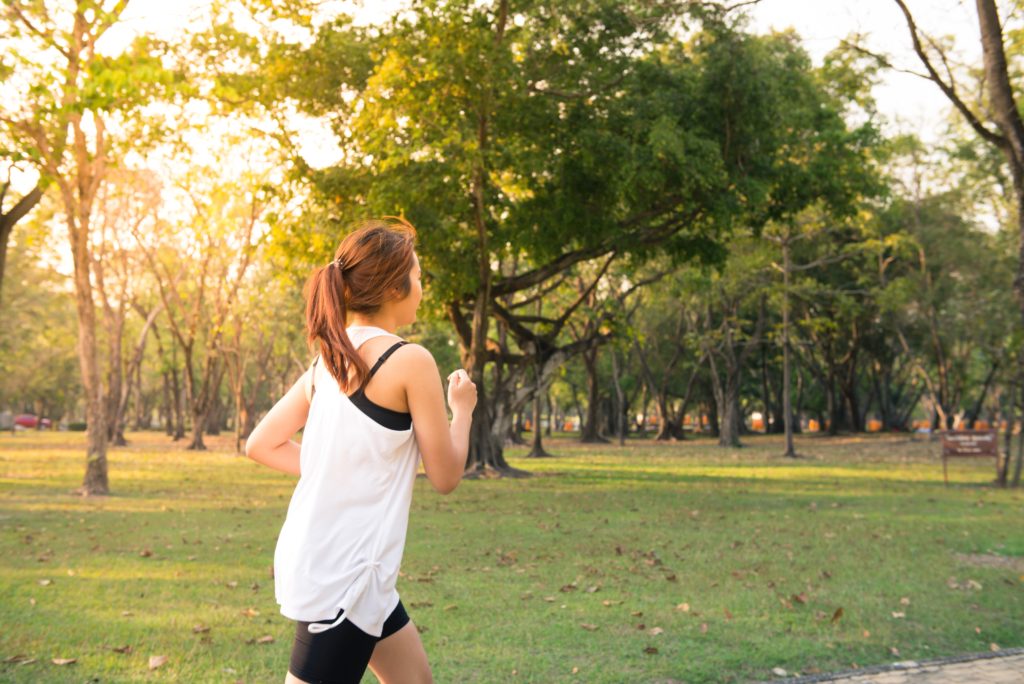 Frau joggt durch grünen Park Physiotherm